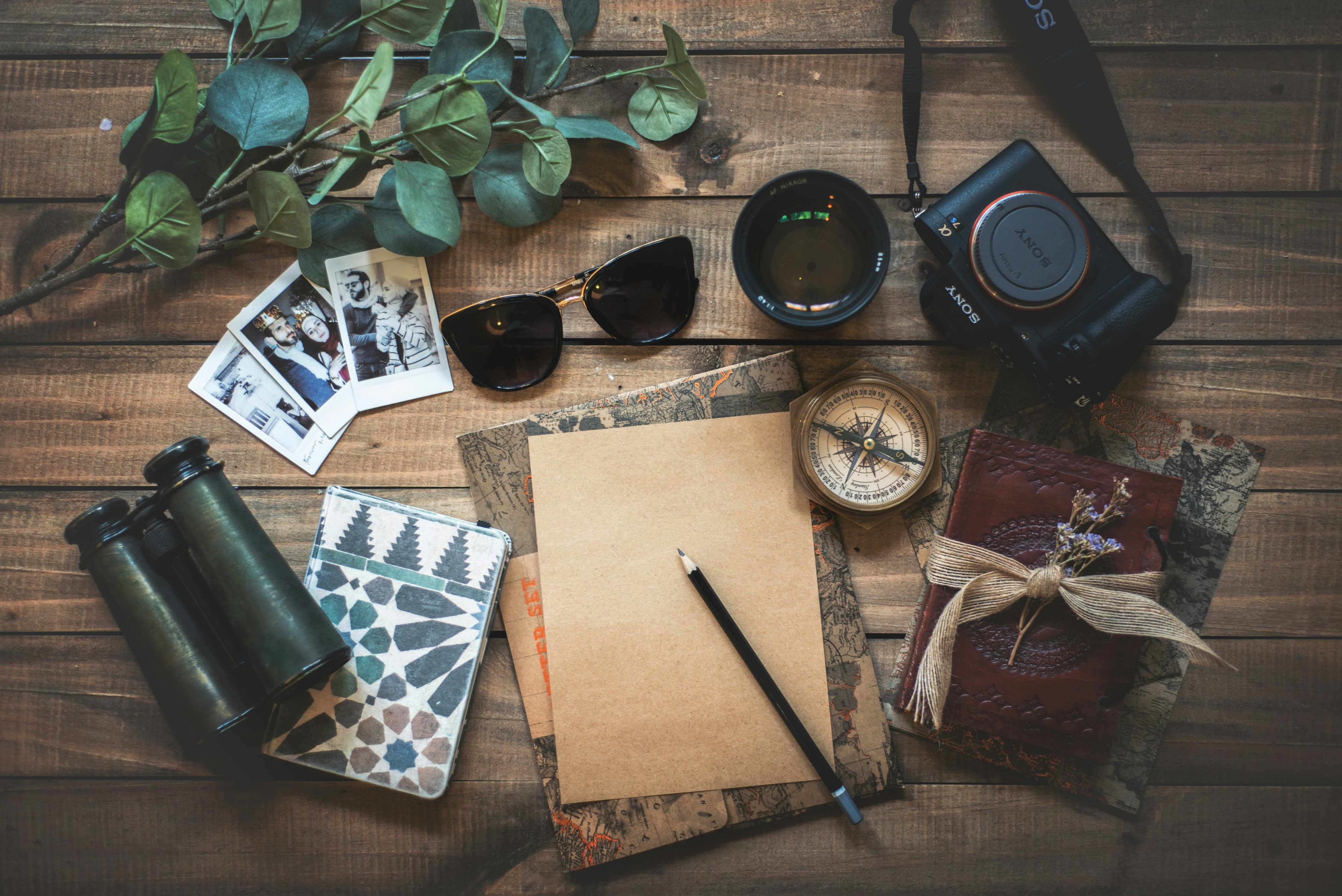 Travel notebook, camera and sunglasses laid out on a wooden table